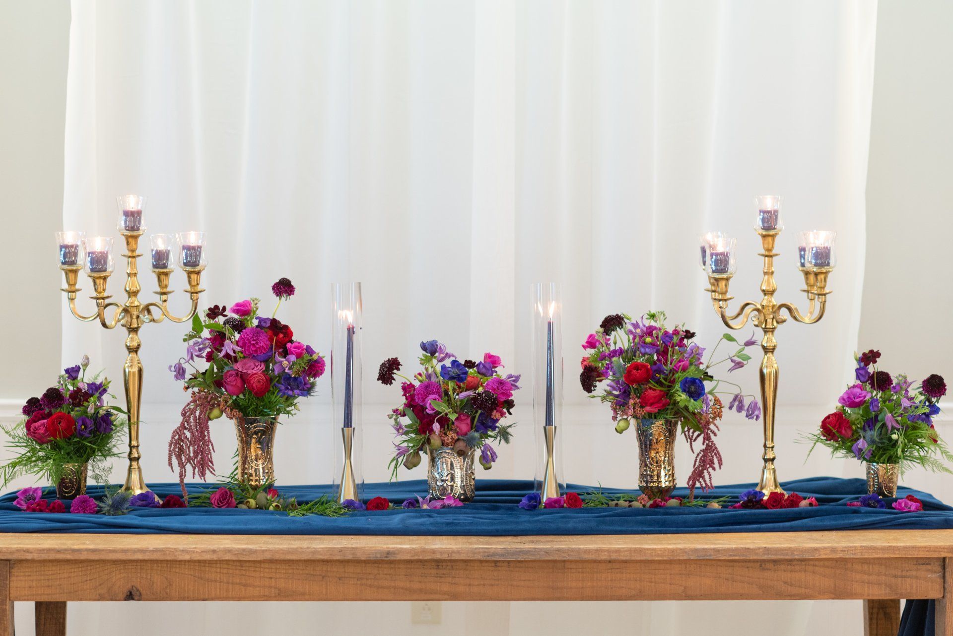 Decorative table with colorful flower arrangements and gold candelabras against a white backdrop