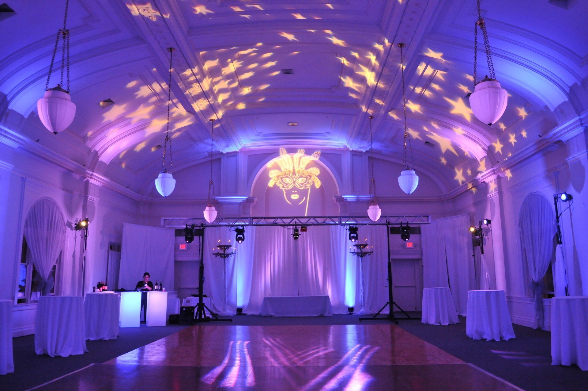 Lavender-lit banquet hall with draped tables, dance floor, and decorative ceiling lighting
