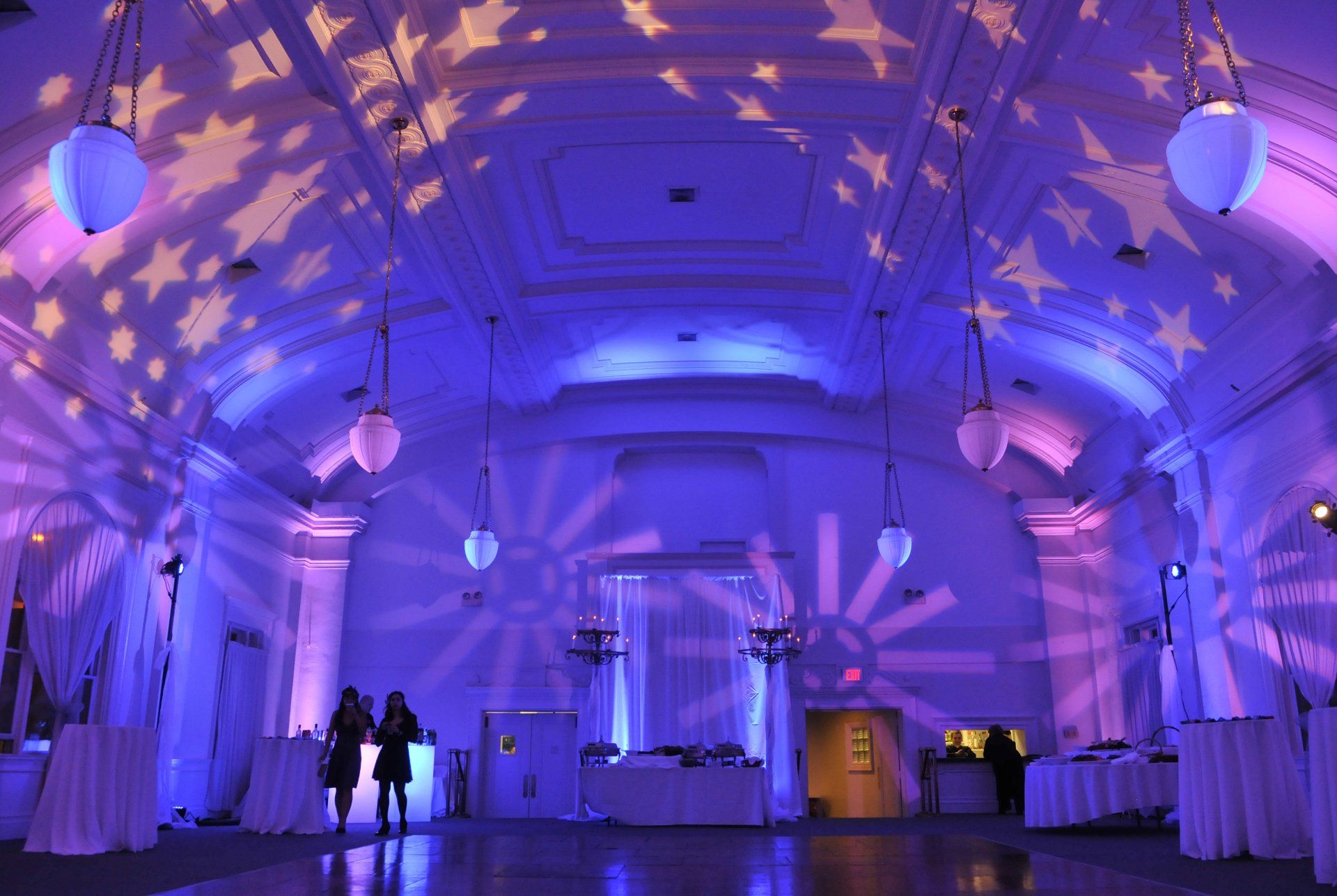 Purple-lit hall with hanging lanterns and star projections, with a few people standing near the left side