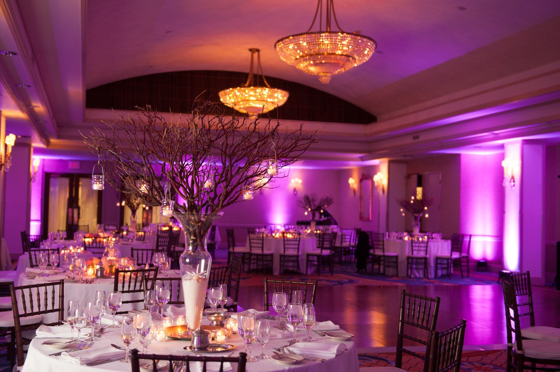 Lavishly lit banquet hall with round tables, chandeliers, and purple accent lighting