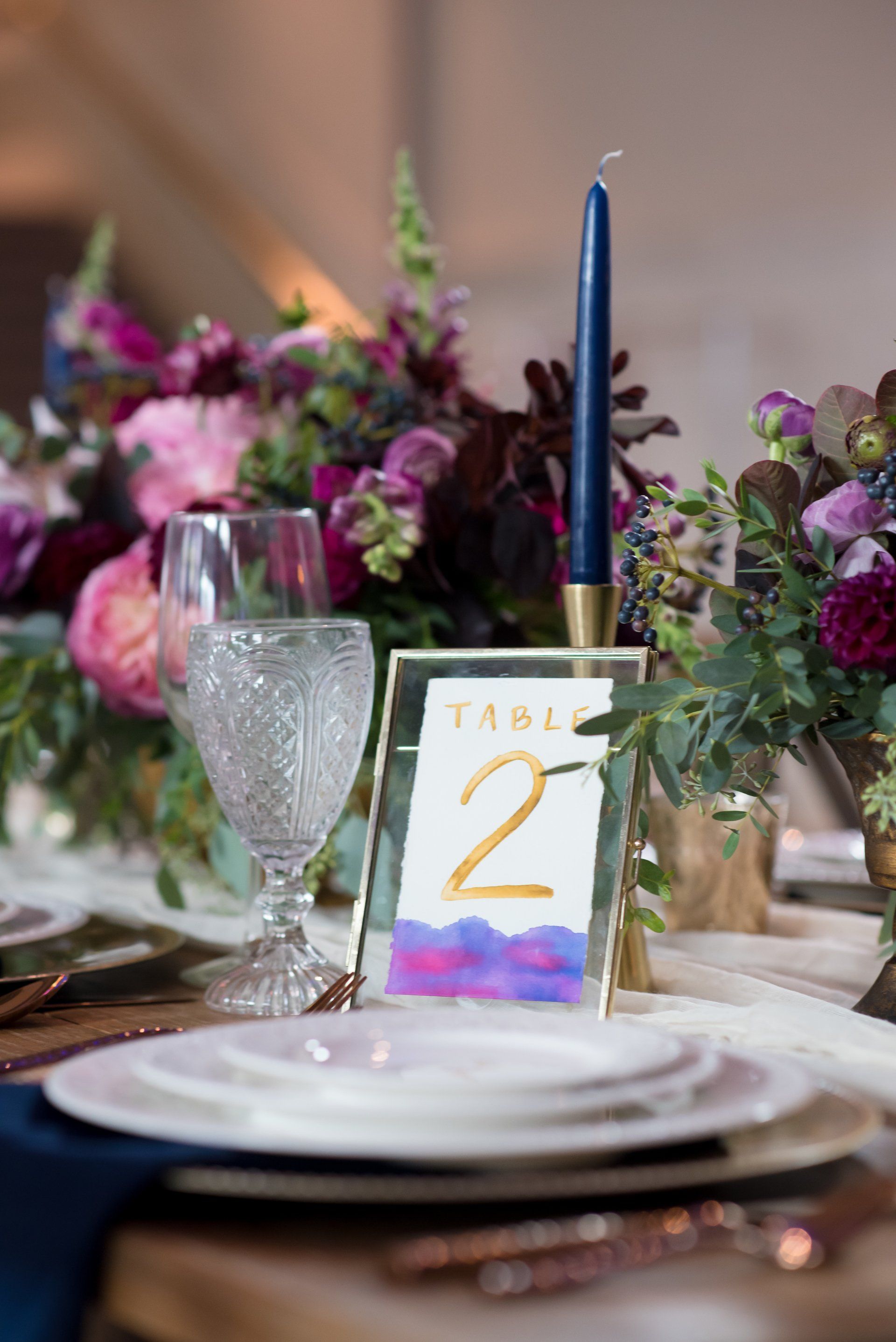 Table 2 card with blue candle on a floral-decorated dining table with plates and glassware