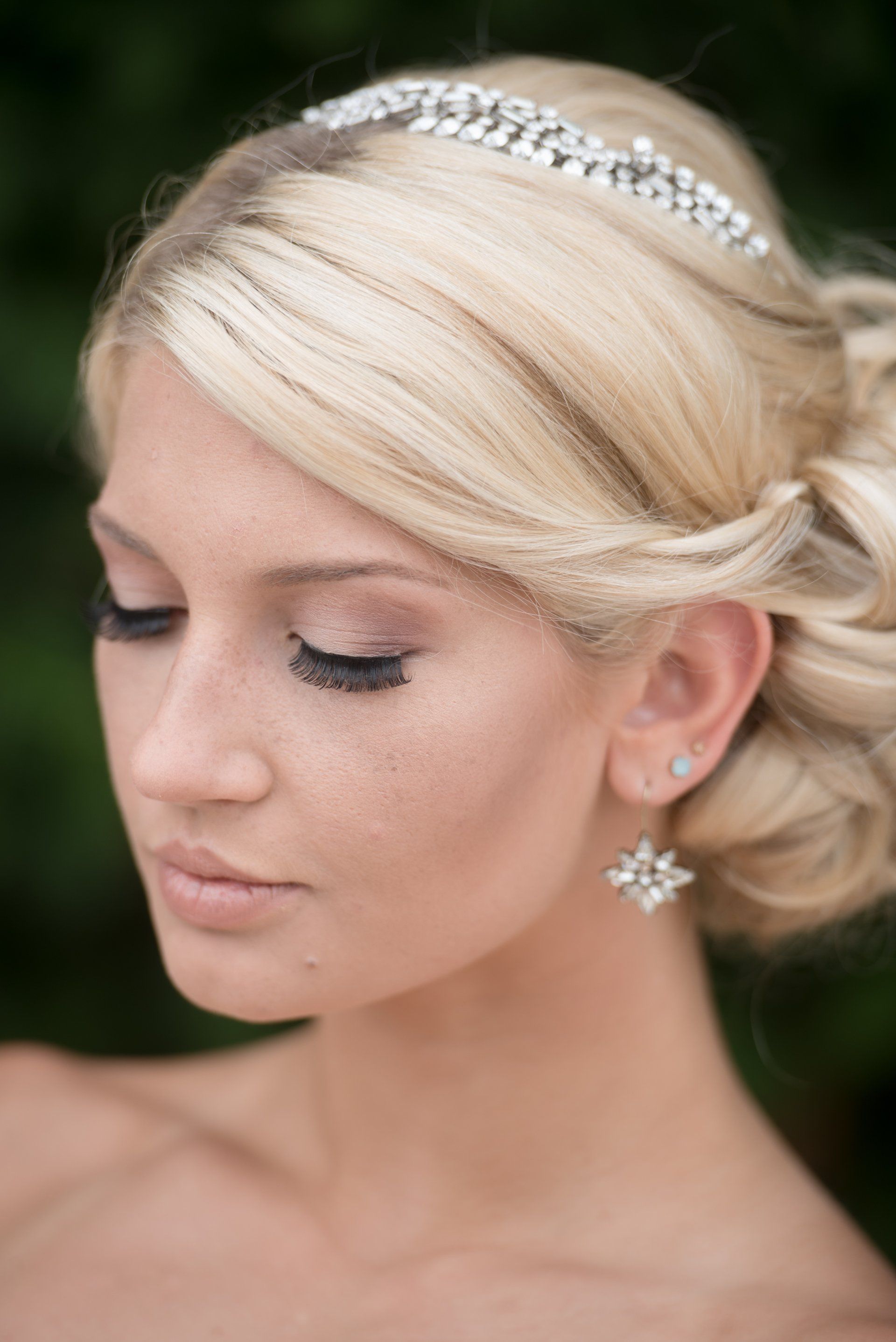 Bride with jeweled headband and earrings, eyes closed, in a soft outdoor portrait