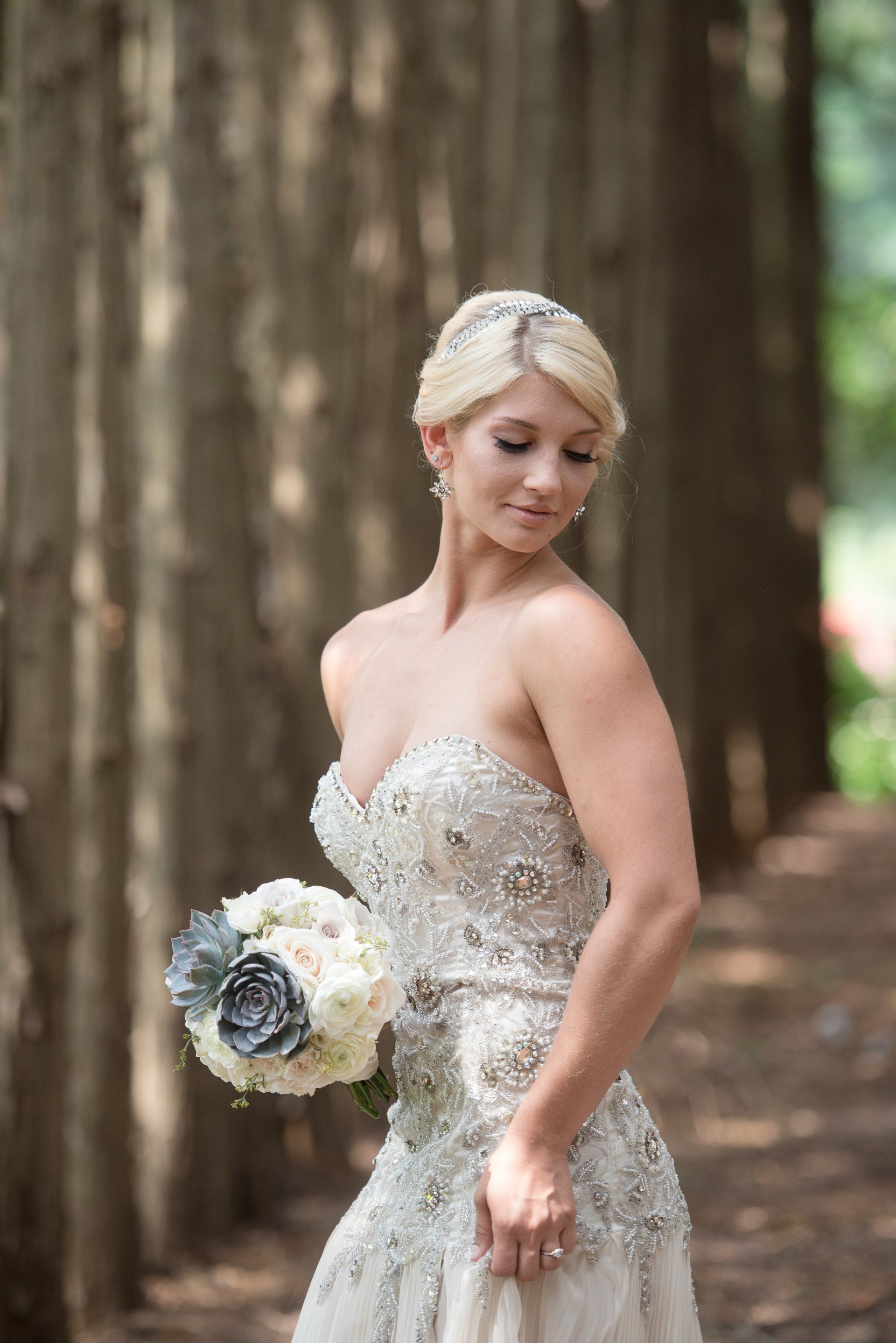 Bride in a sparkling gown holding a bouquet in a wooded outdoor setting