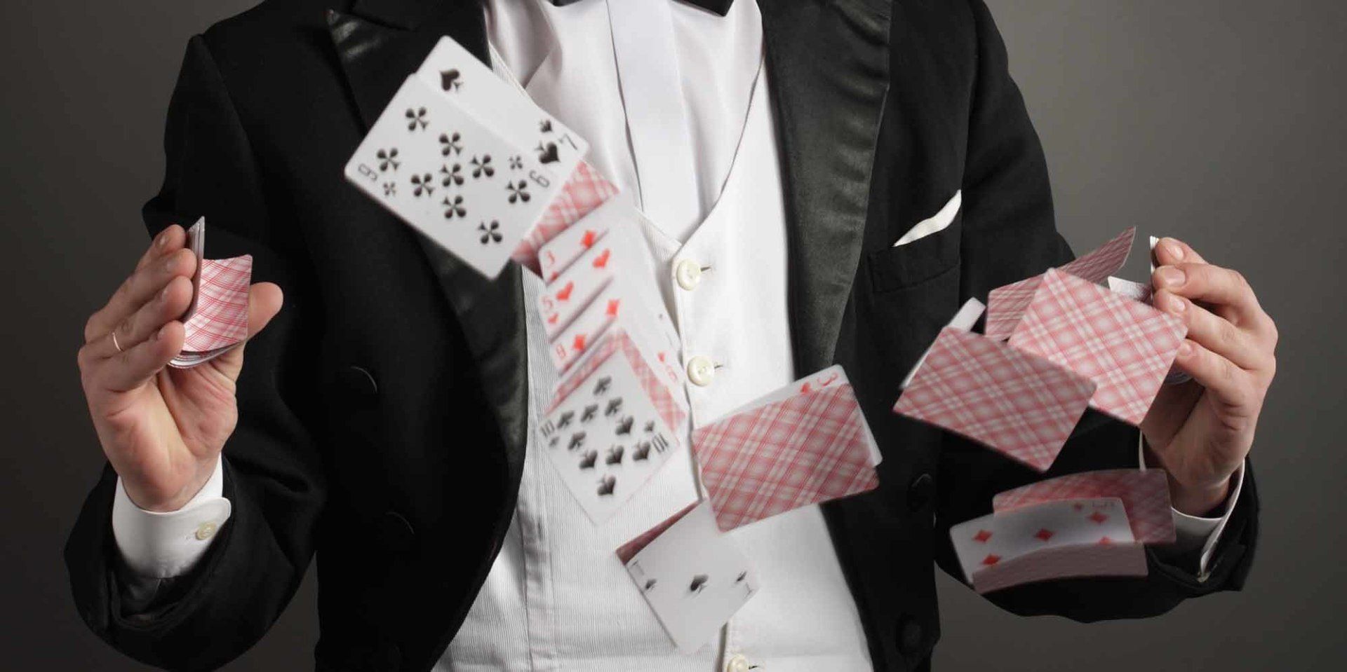 Magician in tuxedo juggling playing cards midair against a dark background