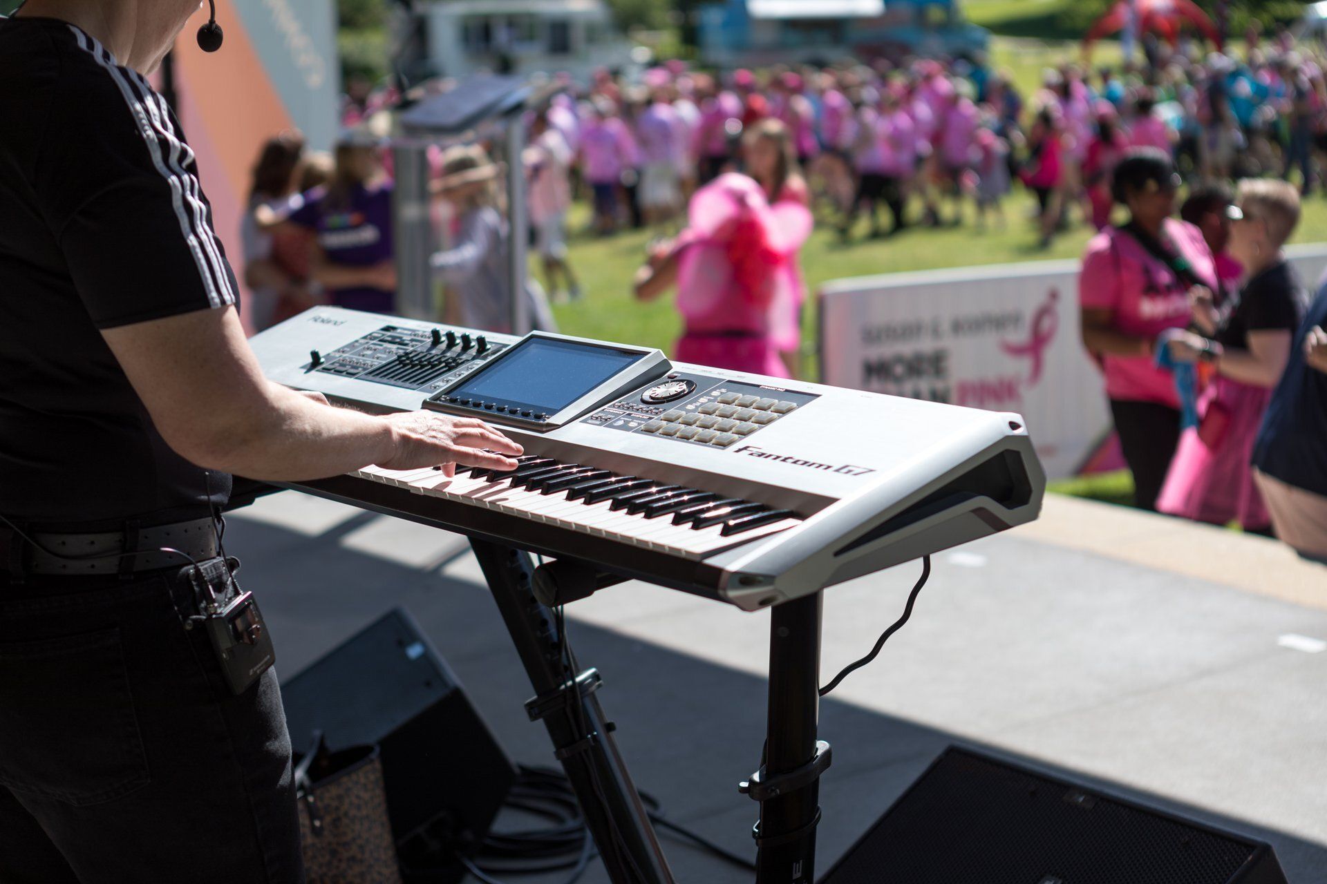 Musician playing keyboard onstage at an outdoor event with a crowd in the background