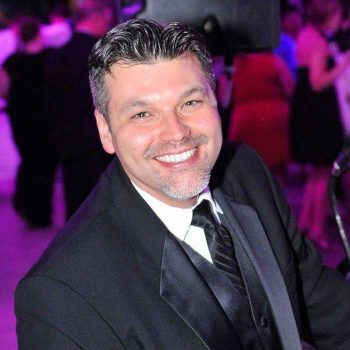 Smiling man in a black suit and tie at a purple-lit event