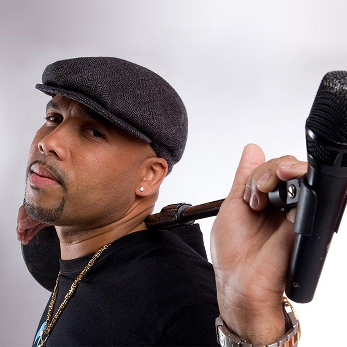 Man in a gray cap holding a microphone over his shoulder, facing the camera