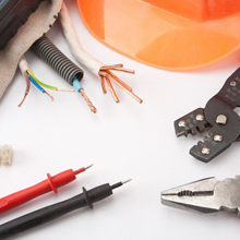 Electrical supplies including copper wires, crimping pliers, multimeter probes, and an orange hard hat on white background.