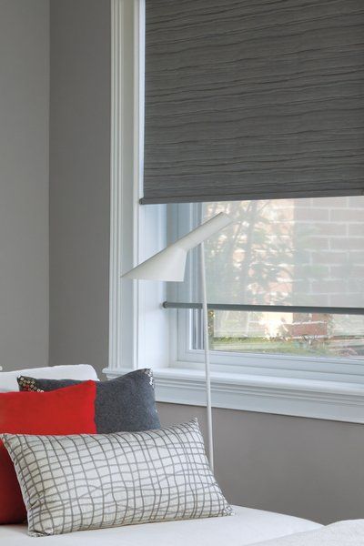 A bedroom with a bed , pillows , a lamp and a window with blinds.