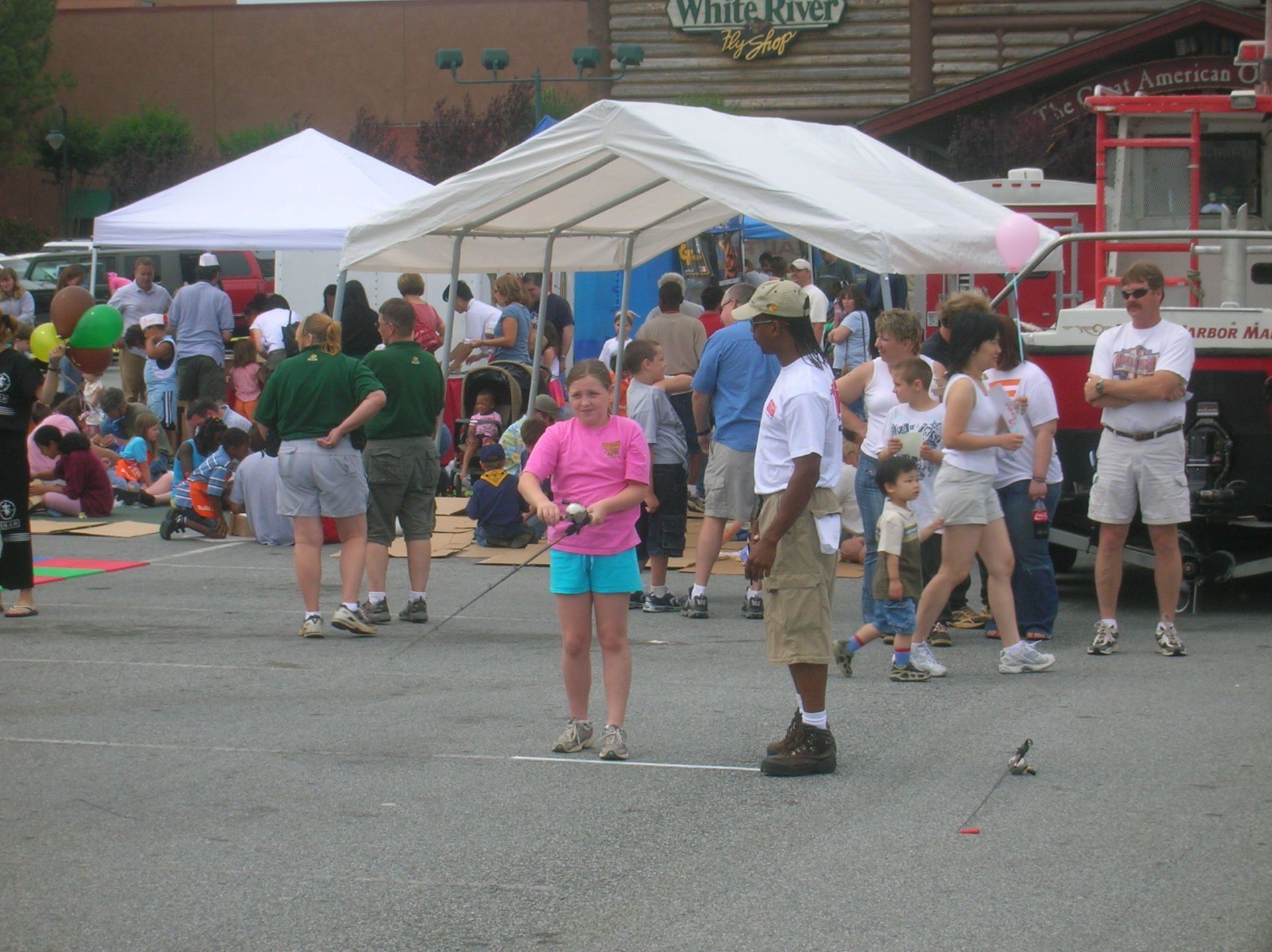 Girl in pink shirt and boy playing a game at an outdoor fair, tents in the background.