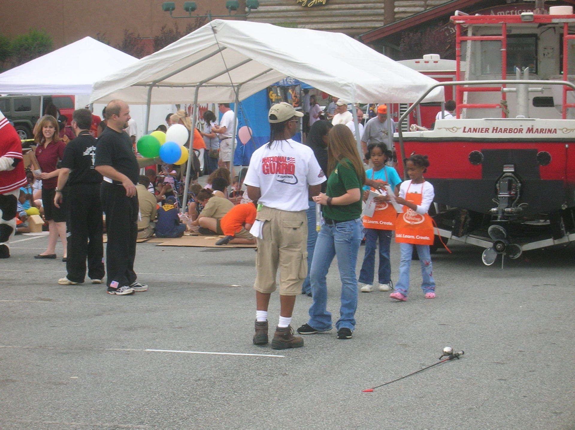 People at an outdoor event with a tent, fire truck, and children wearing aprons.