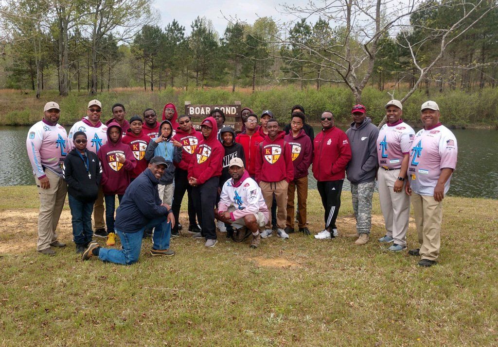 Group of people in red hoodies pose near a pond and trees.