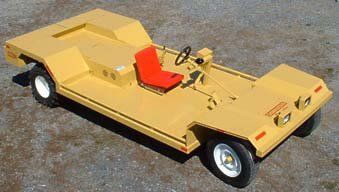Yellow industrial cart with a red seat, steering wheel, and headlights on an asphalt surface.