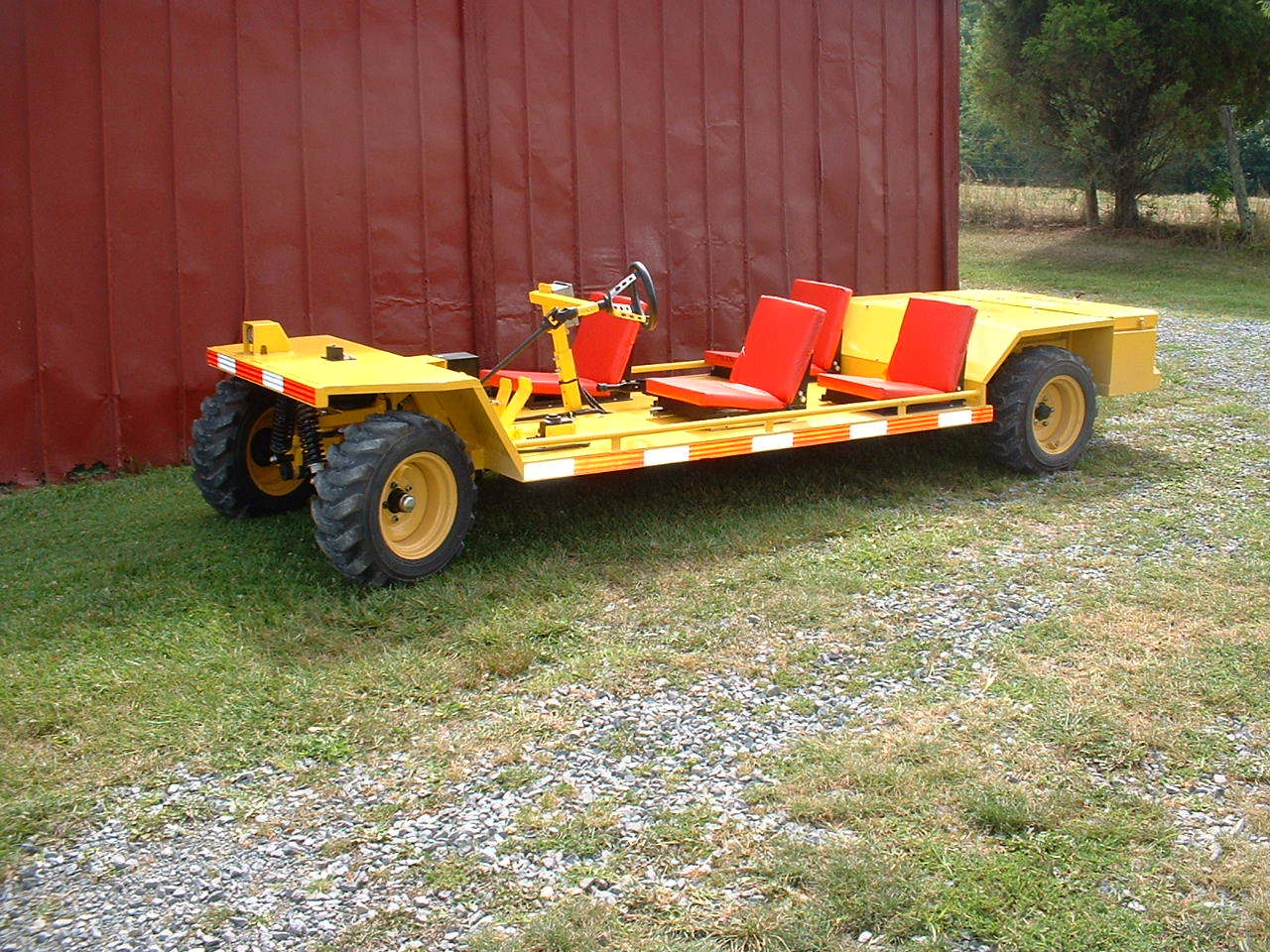 Yellow, open-air vehicle with three seats, parked on grass next to a red barn.
