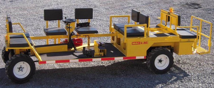 Yellow industrial vehicle with seats, platform, and wheels on a gravel surface.