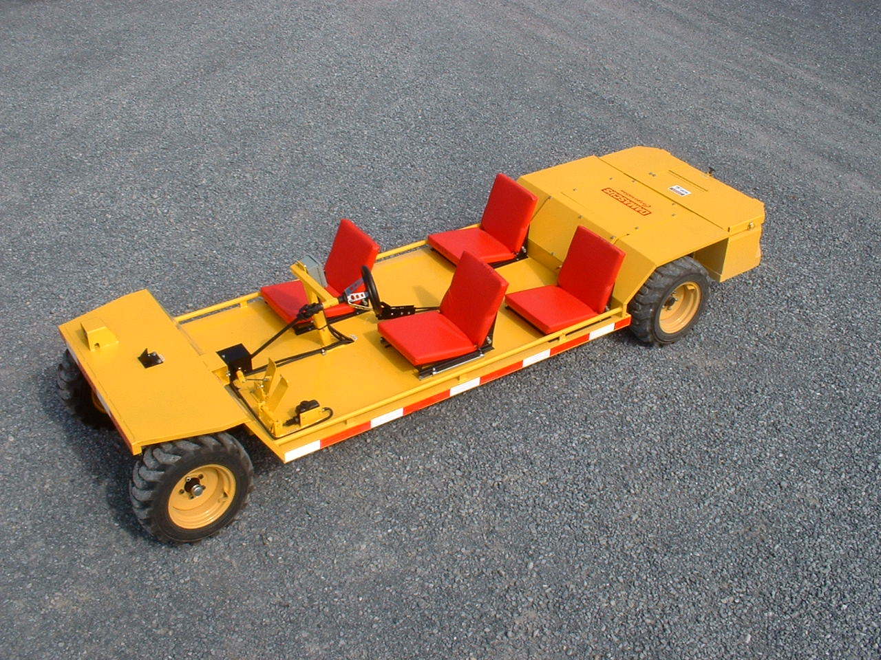 Yellow industrial people mover with red seats, driving on gravel.