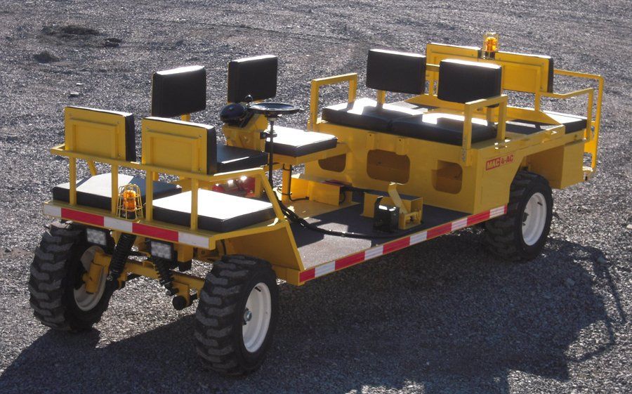 Yellow utility vehicle with seats and a safety railing, on a gravel surface.