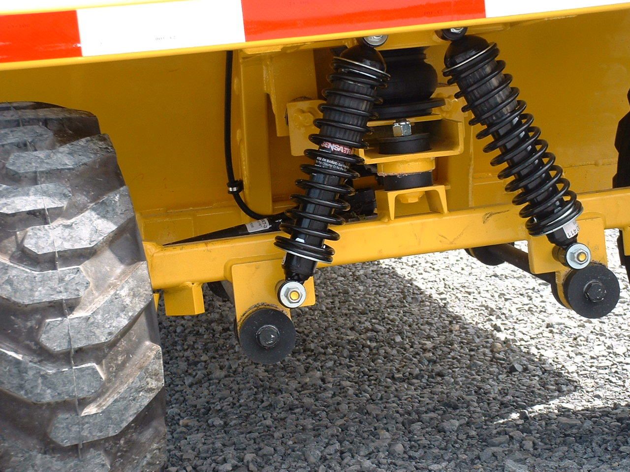Yellow industrial vehicle with black shock absorbers and a large tire.