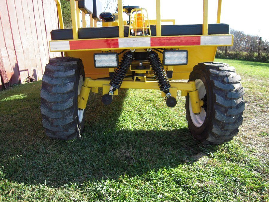 Yellow utility vehicle rear view with large tires, reflective tape, and LED lights.