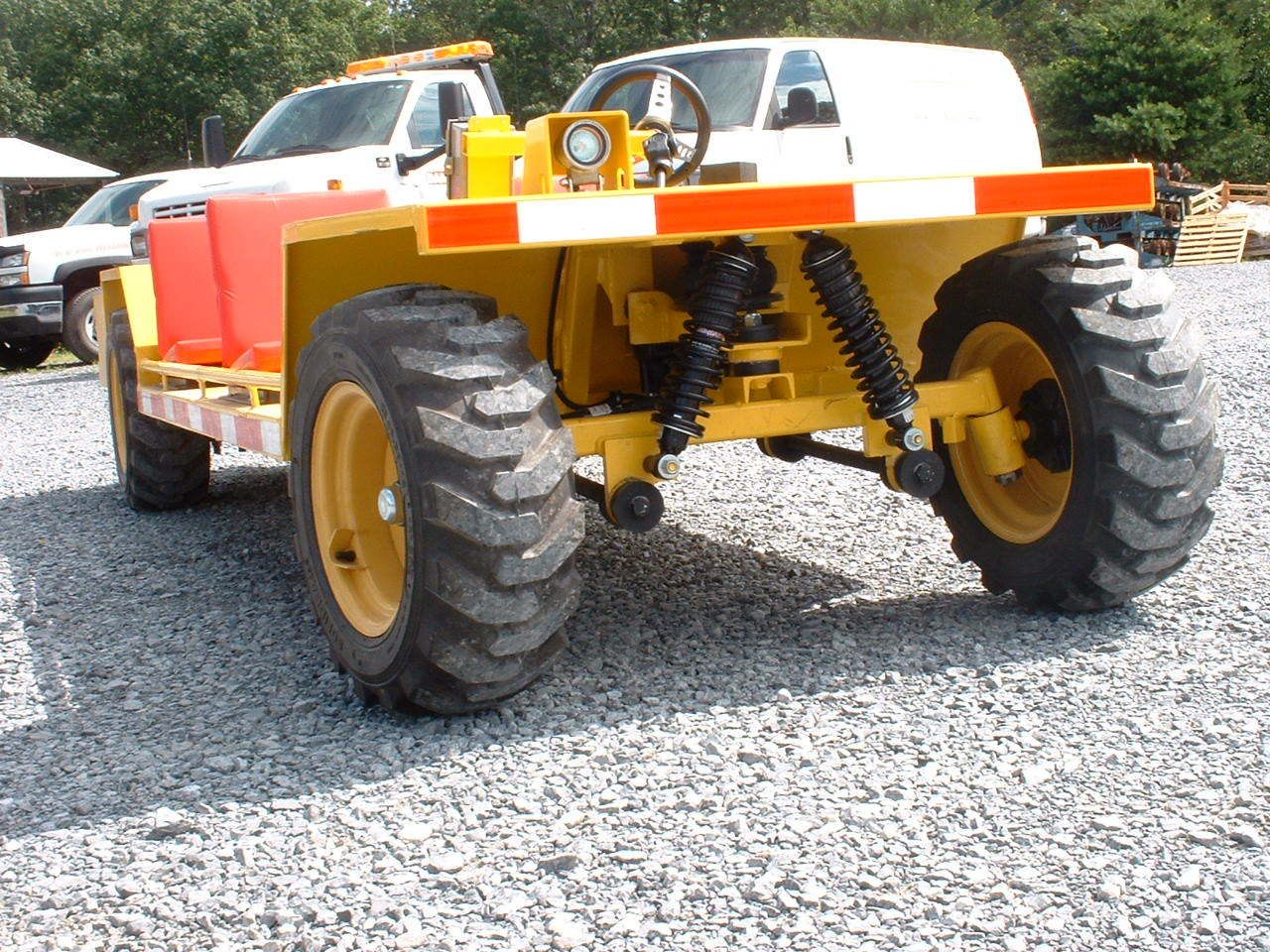 Yellow off-road vehicle with large tires and a flatbed, parked on gravel. Reflective striping.