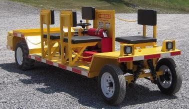 Yellow rail maintenance cart with seating, reflectors, and a fire extinguisher on gravel.