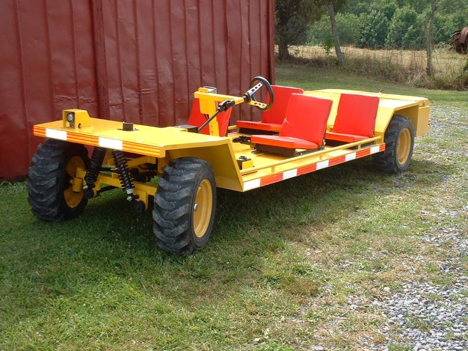 Yellow, open-air utility vehicle with large tires, red seats, and reflective striping, parked on grass.