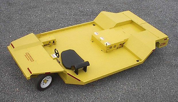 Yellow industrial pull-behind mower with black seat and white wheel, sitting on asphalt.