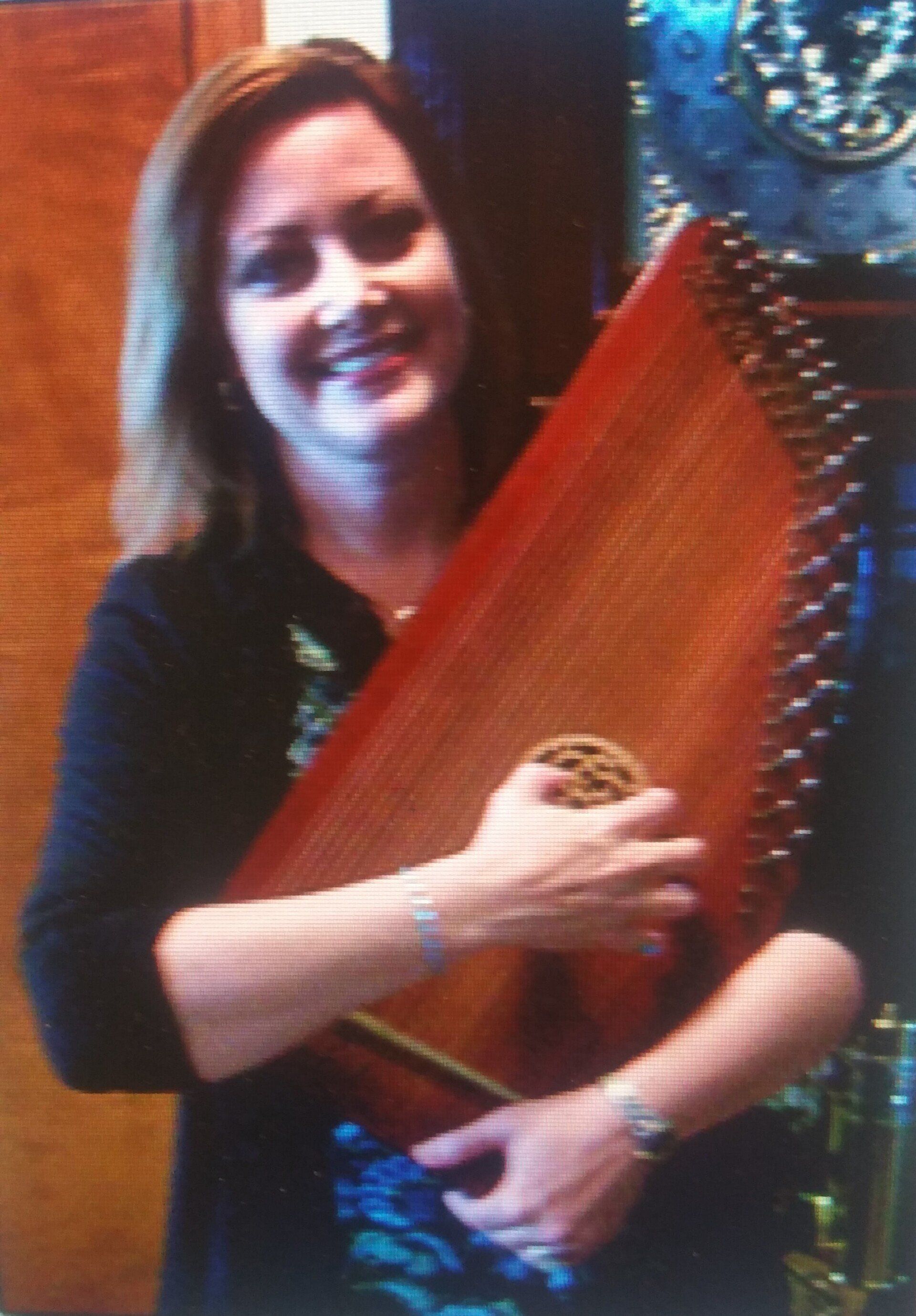 A woman is holding a harp in her hands and smiling.
