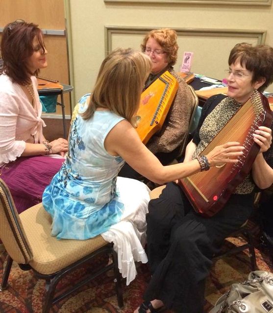 A group of women are sitting around a table with one woman playing a harp