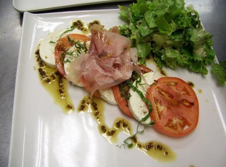 A white plate topped with tomatoes mozzarella and ham