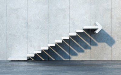 White stairs with arrow at the end on concrete wall, casting long shadow, representing growth and upward direction.