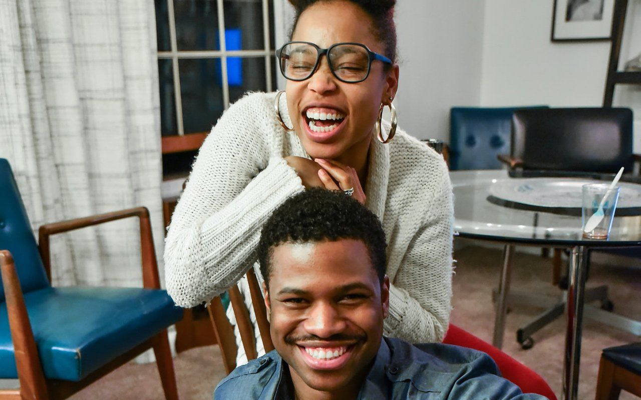 A woman is putting her hand on a man 's head and smiling.