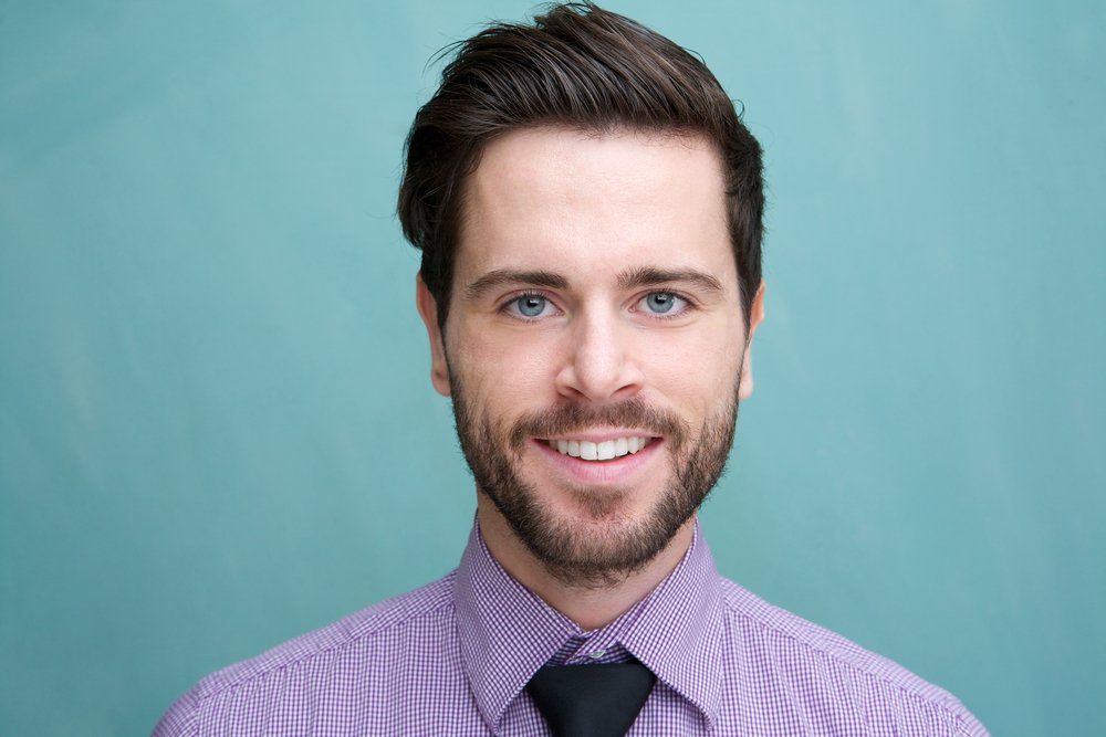 Smiling man in a purple shirt and black tie against a teal background
