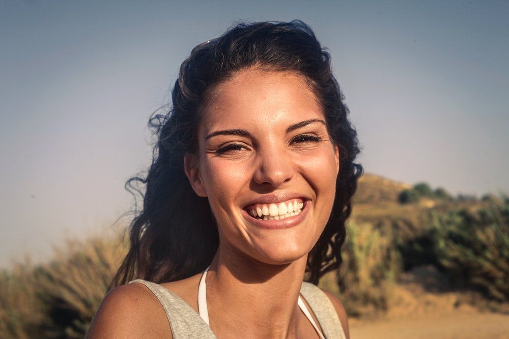 Smiling woman outdoors in warm sunlight with a blurred field in the background