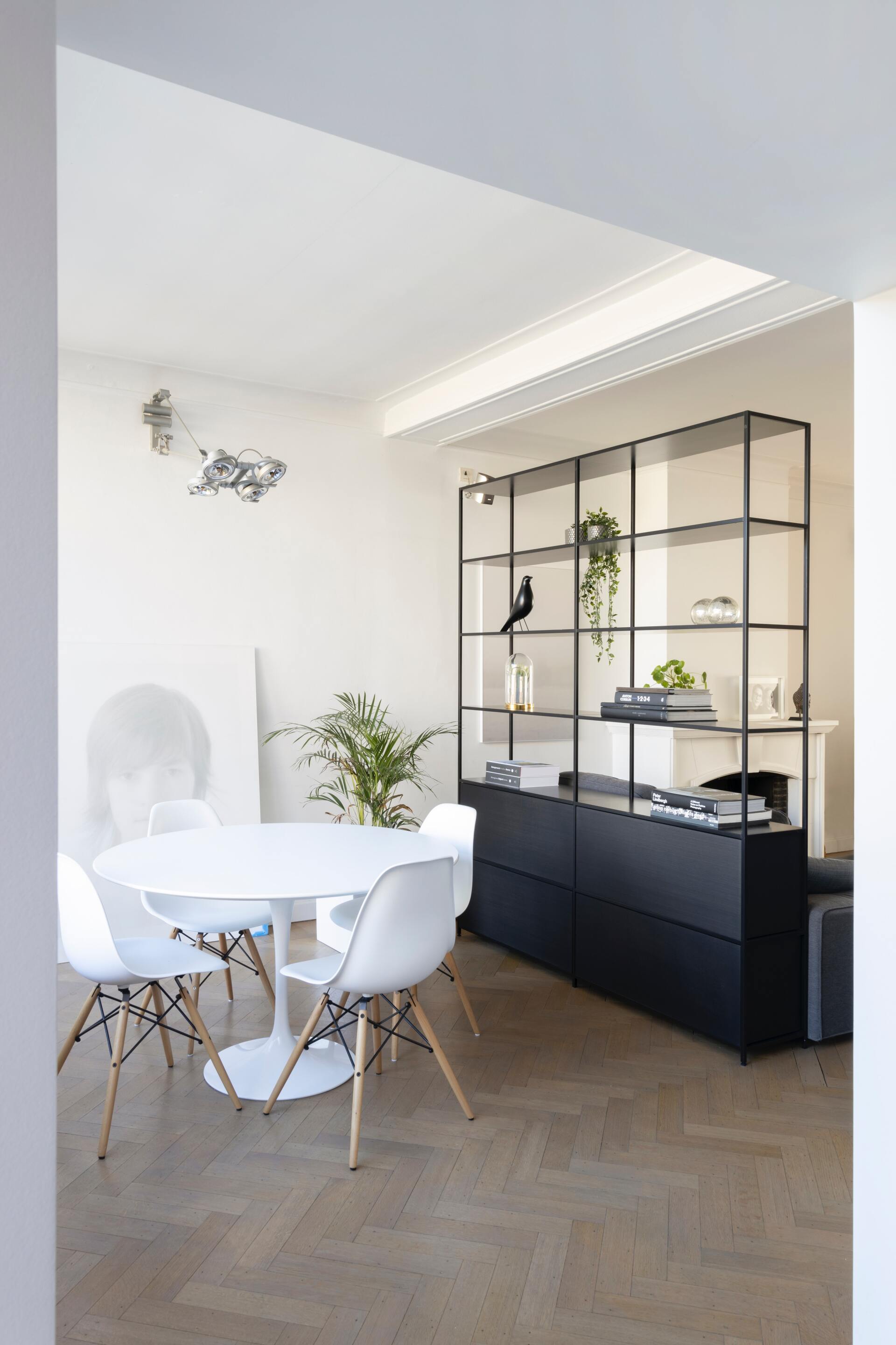 Witte eethoek met ronde tafel en stoelen, zwarte wandkast en planten.