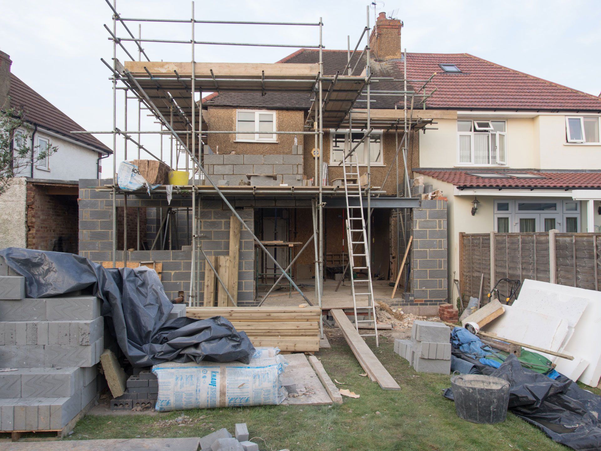 Huis in aanbouw met steigers, muren van betonblokken en bouwmaterialen in de tuin.
