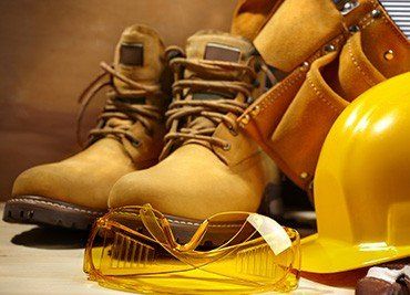 Botas de trabajo, gafas de seguridad transparentes y un casco amarillo sobre una superficie de madera.