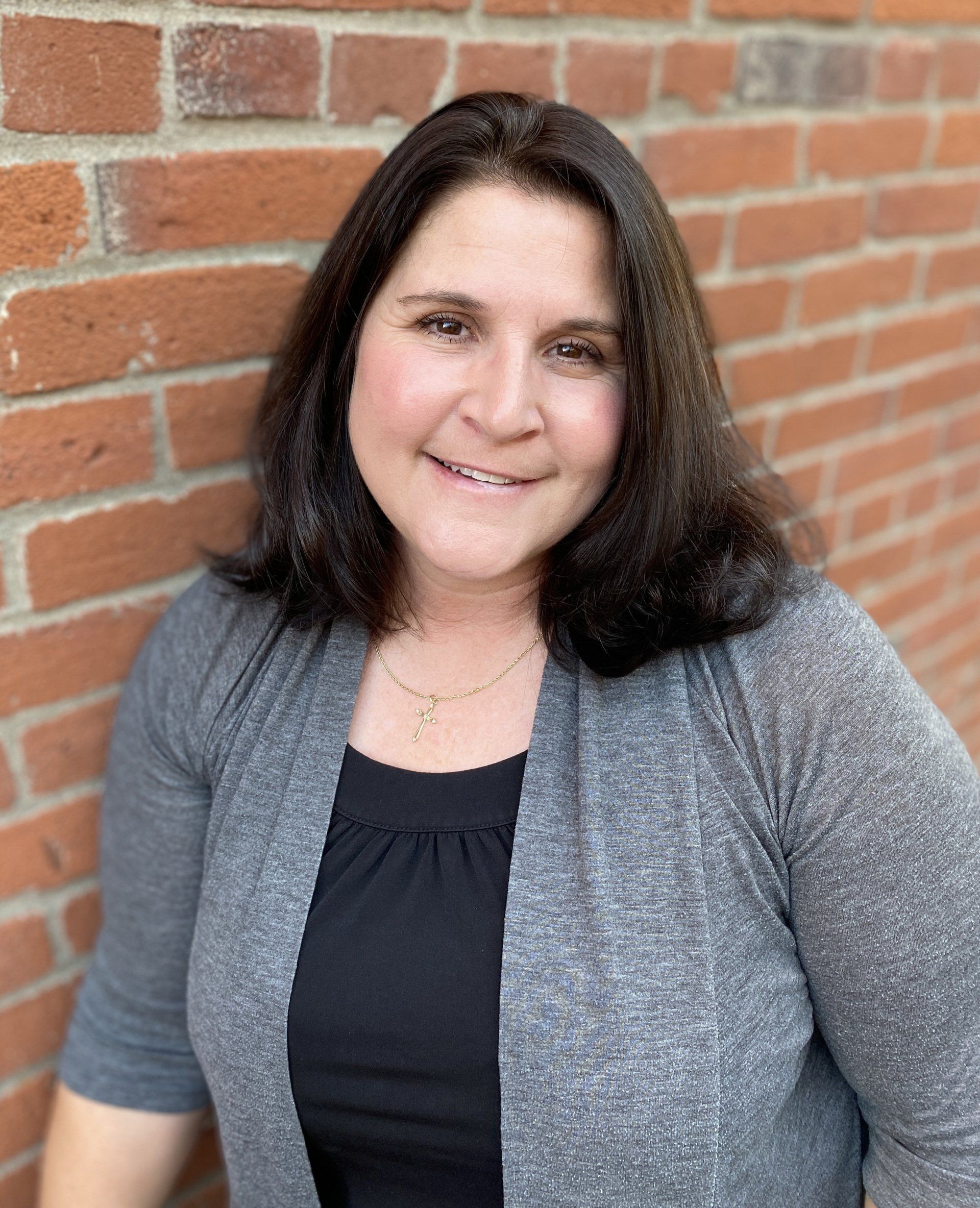 Smiling woman in a gray cardigan standing against a brick wall