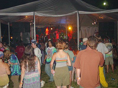 A group of people are dancing under a tent at night
