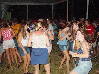 A group of people are dancing in a tent at night. One girl looks terrified.