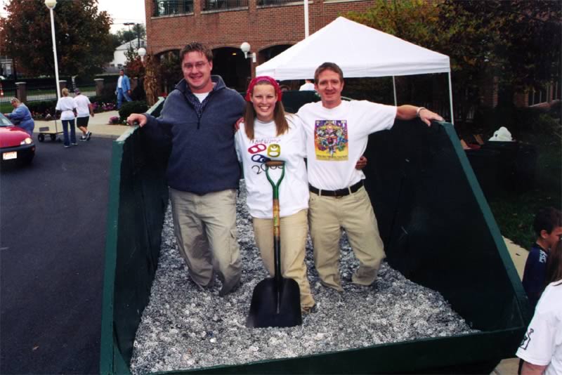 A woman holding a shovel is standing next to two men in a huge pile of aluminum can tabs