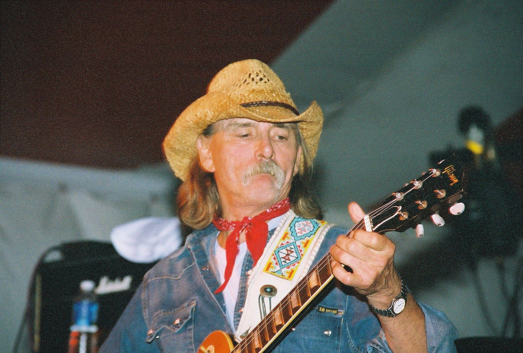 A man in a cowboy hat is playing a guitar. This man is Dickey Effing Betts.