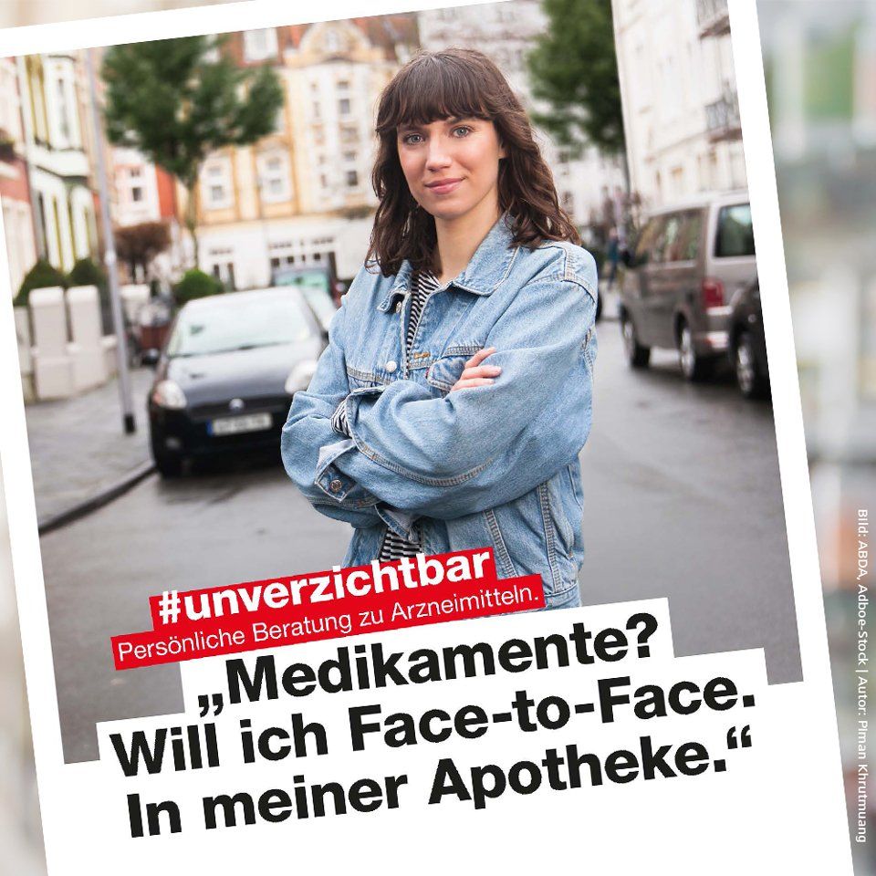 Eine Frau in einer Jeansjacke steht mit verschränkten Armen auf der Straße.