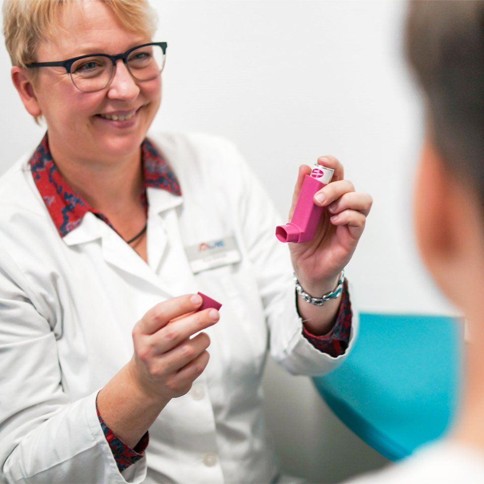 Eine Frau im weißen Kittel hält einen rosa Inhalator