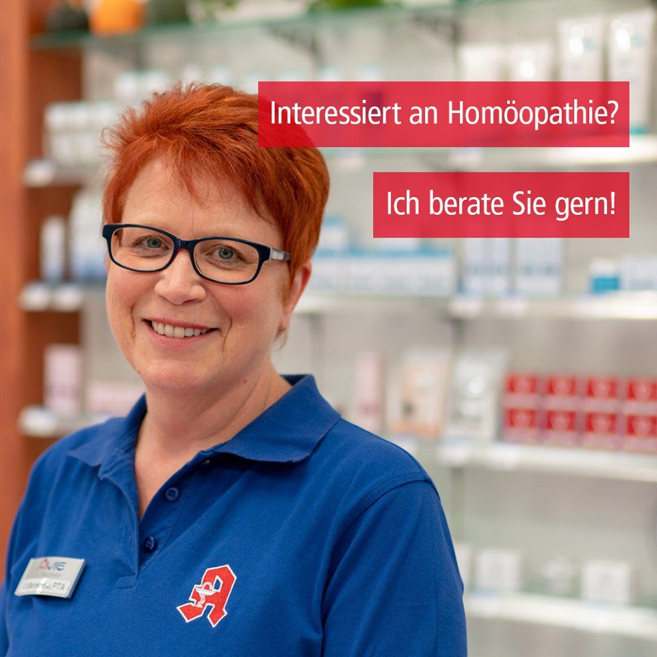 Eine Frau mit Brille und blauem Hemd lächelt vor einem Apothekenregal.