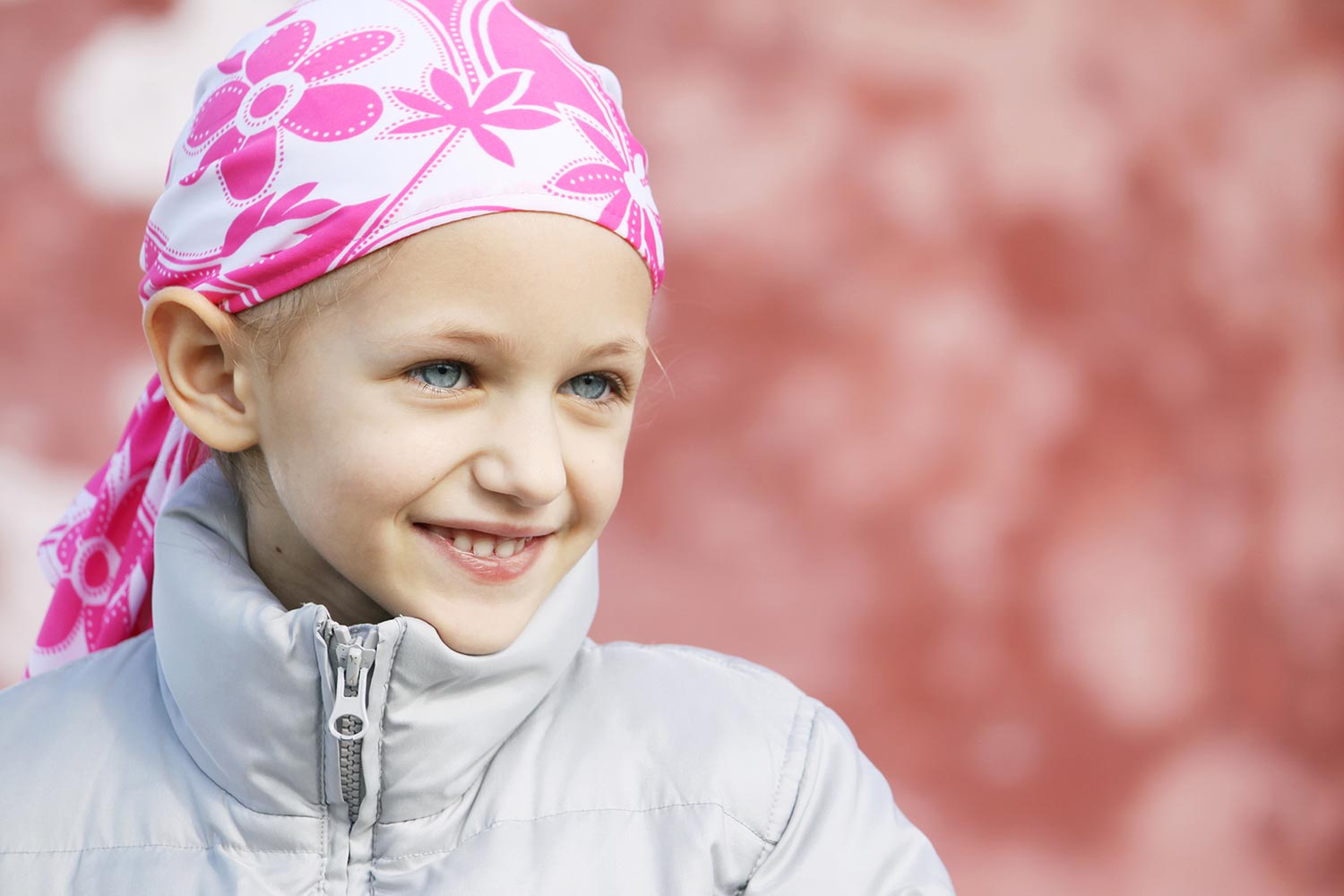 Ein junges Mädchen mit einem rosa Bandana und einer Jacke lächelt.