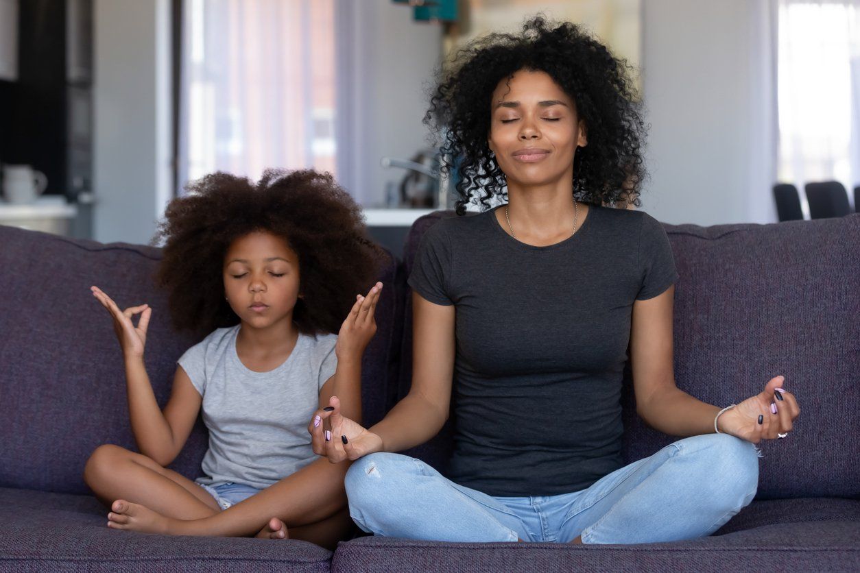 A woman and a child are sitting on a couch meditating.