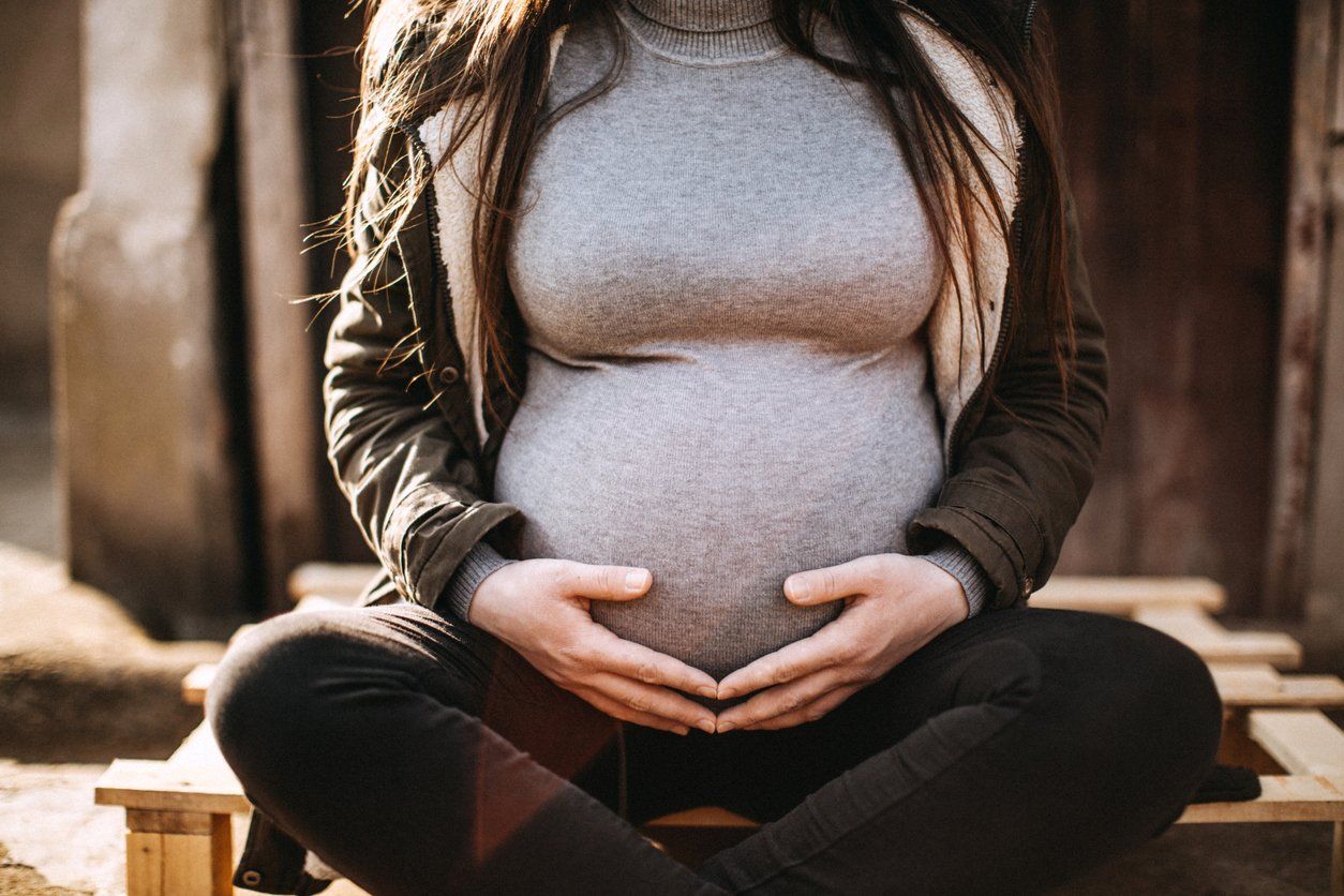 A pregnant woman is sitting in a lotus position with her hands on her belly.
