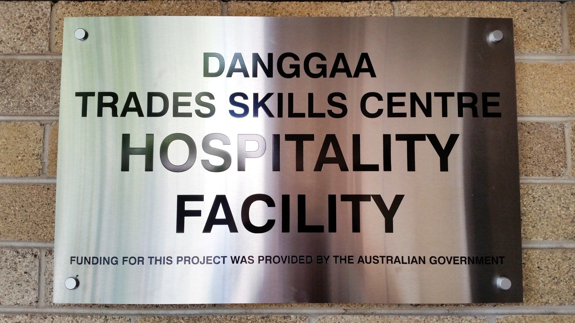 A sign on a brick wall that says ' danggaa trade skills centre hospitality facility '