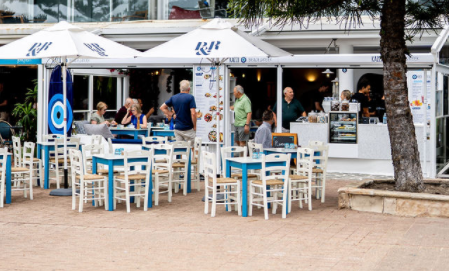 A group of people are sitting at tables outside of a restaurant.